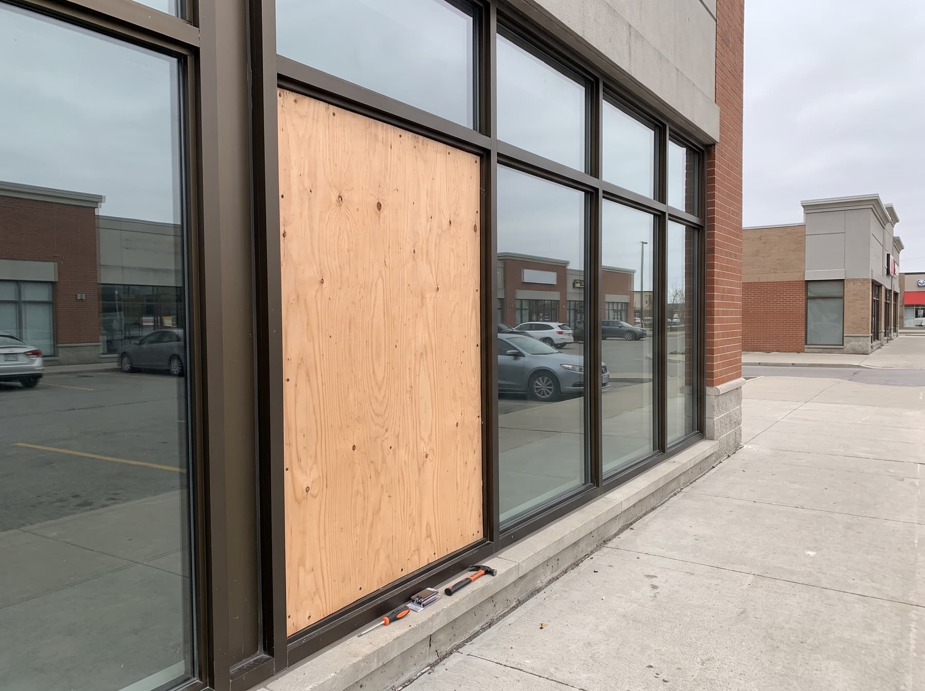 Daytime emergency plywood board-up on a GTA retail plaza storefront after glass breakage